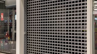 Picture of a silver roller door with gaps, at the front of a closed shop.