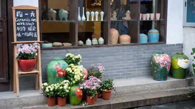 A ceramic art workshop with colourful ceramic pots around the store-front and in the shop window. The store has a 1 metre high concrete brick wall on the outside